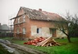 Stary ceglany dom w remoncie, odkryta więźba dachowa i rusztowanie przy ścianie